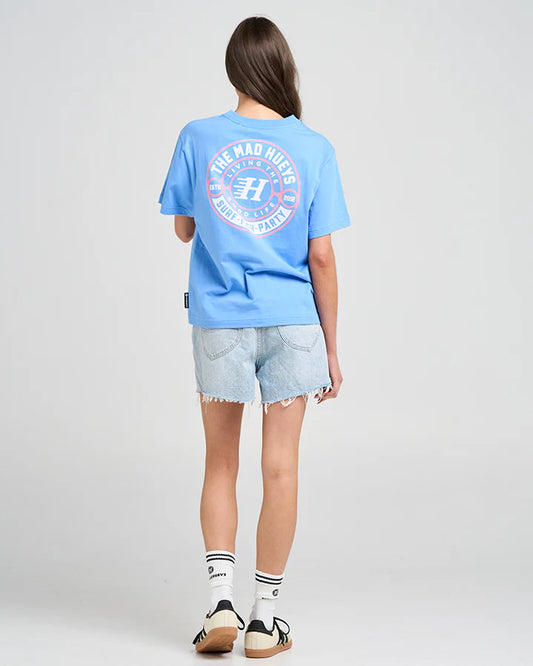 Person wearing a blue t-shirt with a logo on the back, standing against a plain background