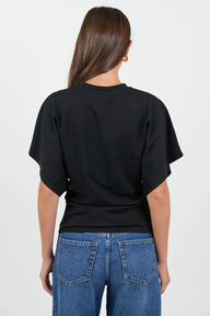 A woman viewed from the back wearing a black short-sleeve t-shirt and blue jeans against a plain light gray background.