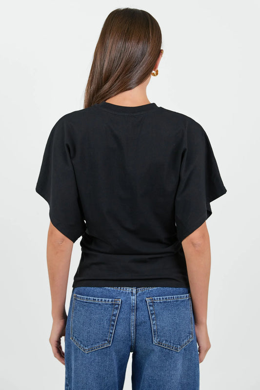 A woman viewed from the back wearing a black short-sleeve t-shirt and blue jeans against a plain light gray background.