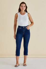 Woman wearing a white sleeveless top and blue jeans against a beige background