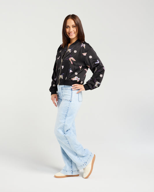 Woman wearing a black floral bomber jacket and light blue jeans on a white background