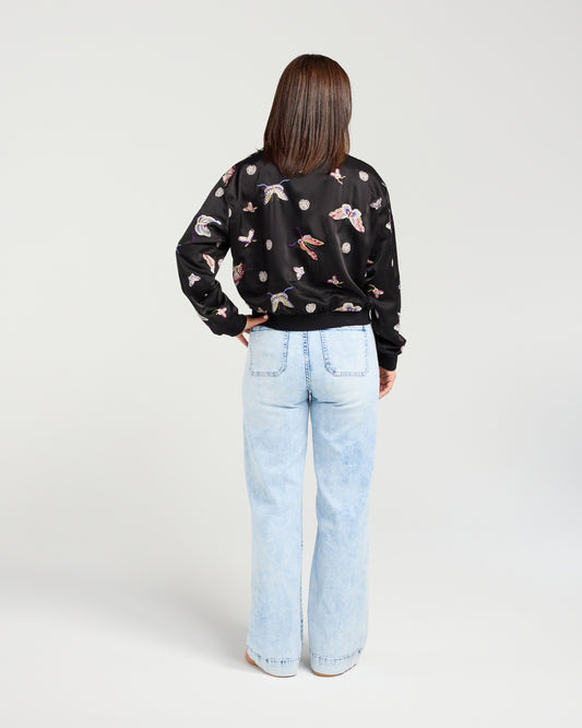 Person wearing a black patterned shirt and light blue jeans on a white background