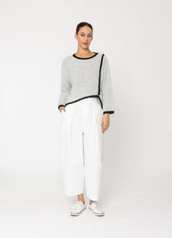 Woman wearing a gray sweater with black trim and white pants on a white background