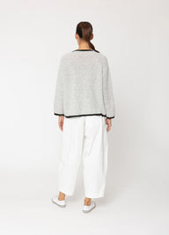 Person wearing a textured sweater and white pants on a white background