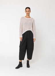Woman wearing a light pink sweater and black pants on a white background