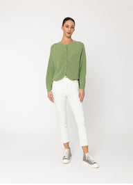 Woman wearing a green cardigan and white pants on a white background