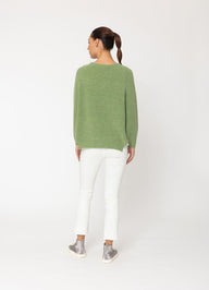Person wearing a green sweater and white pants on a white background