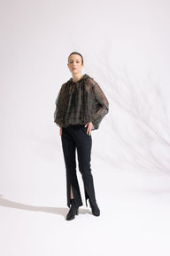 Person wearing a patterned blouse and black pants on a white background