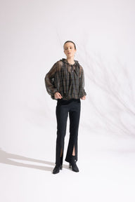 Person wearing a sheer black top with a pattern and black pants on a white background