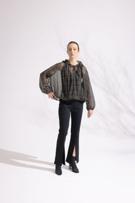 Person wearing a patterned blouse and black pants on a white background