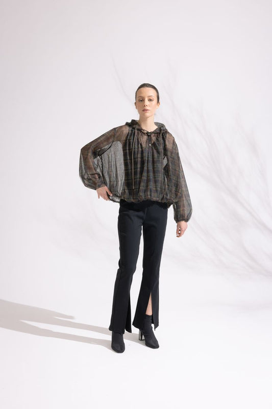 Person wearing a patterned blouse and black pants on a white background