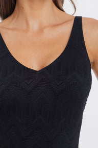 Close-up of a woman wearing a black sleeveless V-neck top with a subtle geometric textured pattern, set against a plain light background.