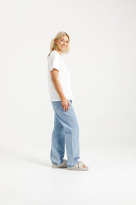Woman wearing Home-Lee Chris Tee in white with a Blossom Berry bow design & blue jeans on a white background