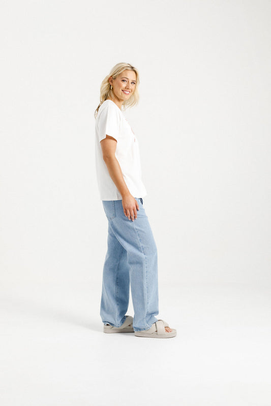 Woman wearing Home-Lee Chris Tee in white with a Blossom Berry bow design & blue jeans on a white background