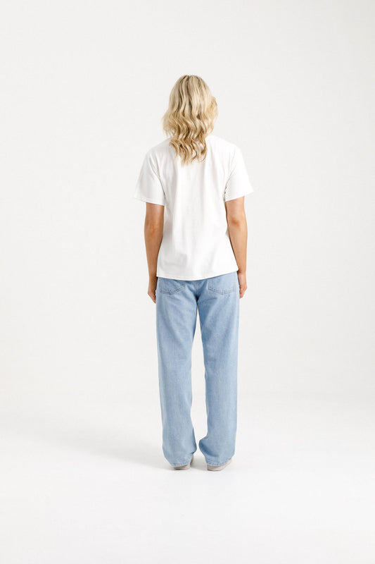 Woman wearing Home-Lee Chris Tee in white with a Blossom Berry bow design & blue jeans on a white background