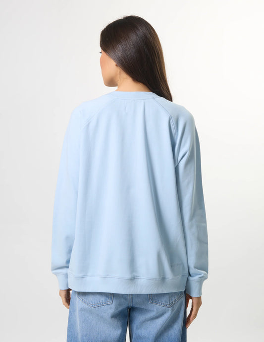 Person wearing a light blue sweatshirt and jeans on a plain background