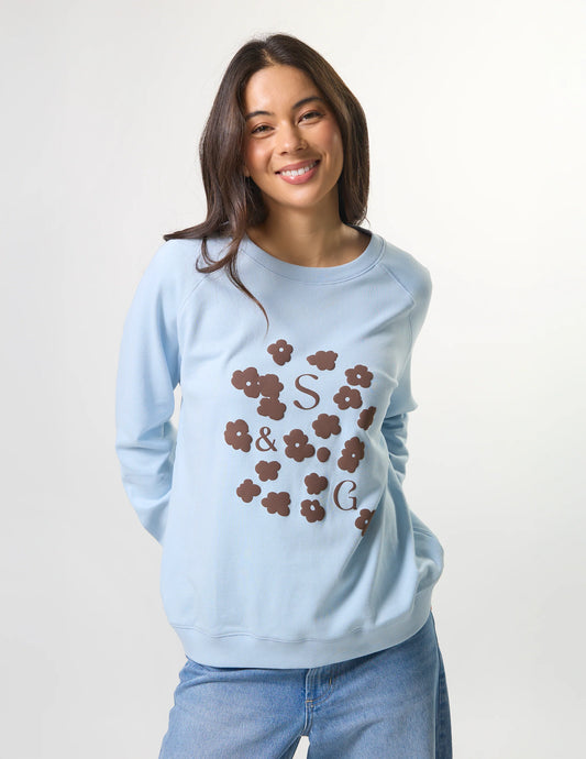 Woman wearing a light blue sweatshirt with floral initials design on a plain background