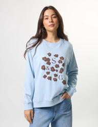 Woman wearing a light blue sweatshirt with floral lettering on a white background