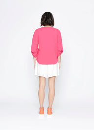 Person wearing a bright pink blouse and white skirt on a white background