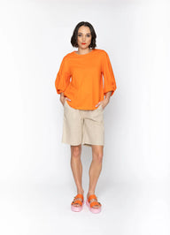 Woman wearing Orange top with Cream shorts and white background