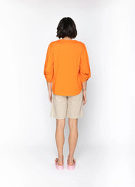 Person wearing an orange shirt and beige shorts on a white background