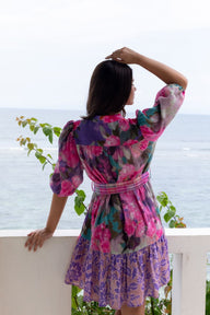 Woman in a colorful floral dress standing by a railing with a scenic background
