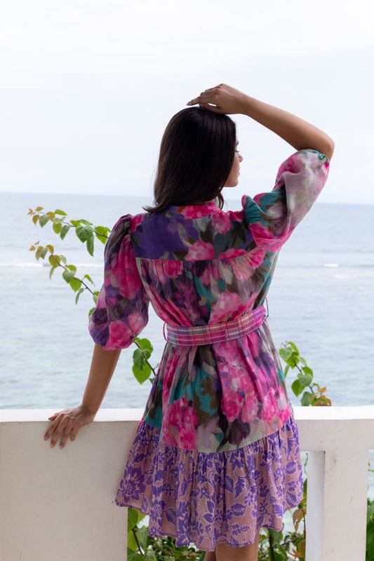 Woman in a colorful floral dress standing by a railing with a scenic background