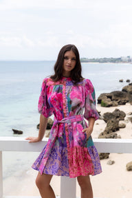 Woman wearing a colorful dress standing on a beach with ocean and rocks in the background