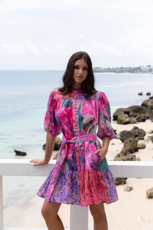 Woman wearing a colorful dress standing on a beach with ocean and rocks in the background