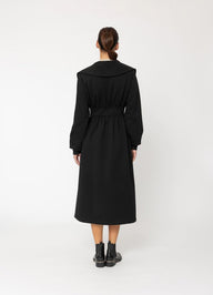 Person wearing a black coat standing against a white background