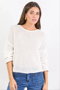 Woman wearing a white textured sweater and blue jeans on a light gray background