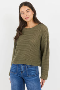 Woman wearing a green textured sweater and blue jeans on a white background