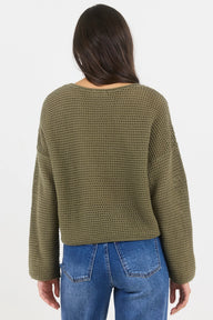 Person wearing a green textured sweater and blue jeans on a white background