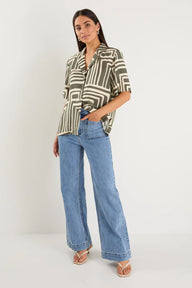 Woman wearing a patterned shirt and blue jeans on a white background