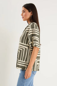 Woman wearing a patterned shirt and jeans on a plain background