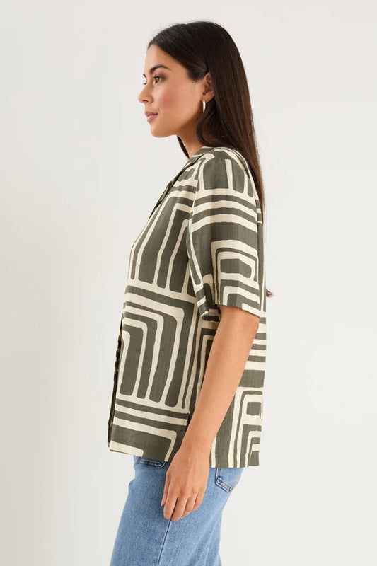 Woman wearing a patterned shirt and jeans on a plain background