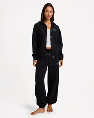 Person wearing a black hoodie and pants with a logo on a white background
