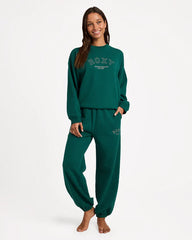 Person wearing a green 'Roxy' sweatshirt and pants on a white background