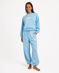 Person wearing a light blue sweatshirt and pants set with a logo on a white background