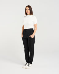 Woman wearing a white top and black pants on a plain background