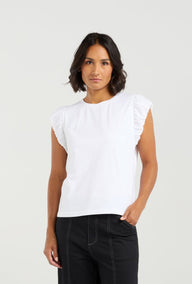 Woman wearing a white sleeveless top with ruffled shoulders against a plain background