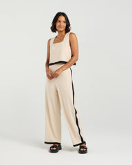 Woman wearing a beige sleeveless top and pants with black trim on a white background
