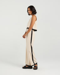 Woman wearing a beige sleeveless top and pants with black trim on a white background
