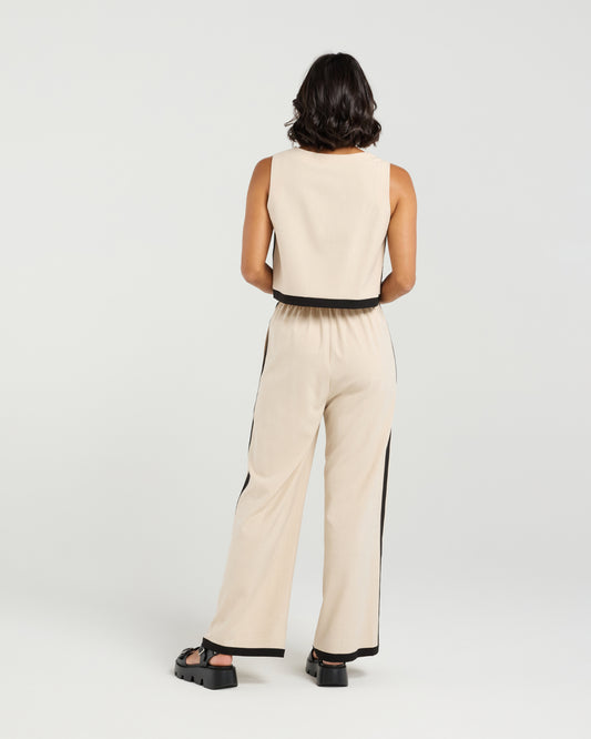 Person wearing a beige sleeveless top and pants with black accents on a white background