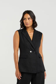 Woman wearing a black sleeveless blazer and wide-leg pants on a white background
