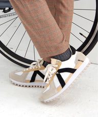 Person wearing beige sneakers with white soles in front of a bicycle wheel.