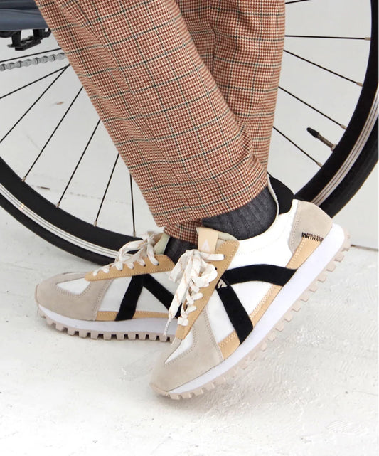 Person wearing beige sneakers with white soles in front of a bicycle wheel.