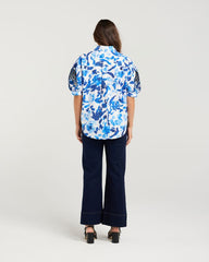 Person wearing a blue floral shirt and dark pants on a white background