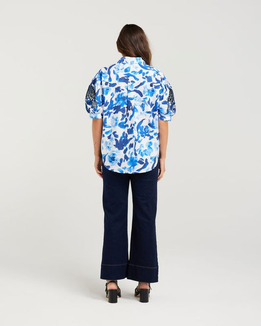 Person wearing a blue floral shirt and dark pants on a white background
