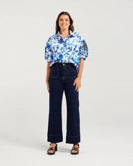 Woman wearing a blue floral blouse and dark blue jeans on a white background
